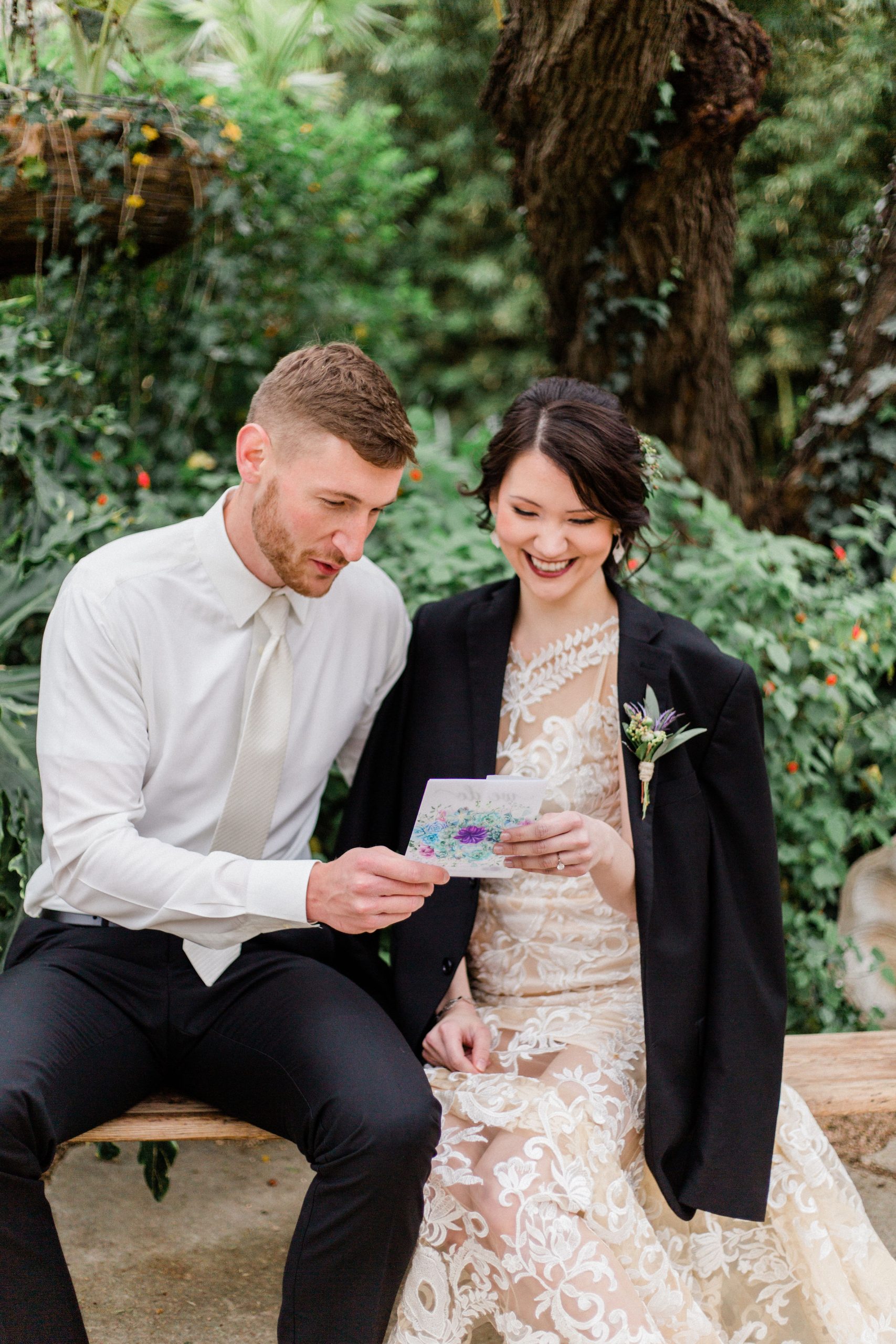 A bride and groom sitting on a bench reading a romantic letter.