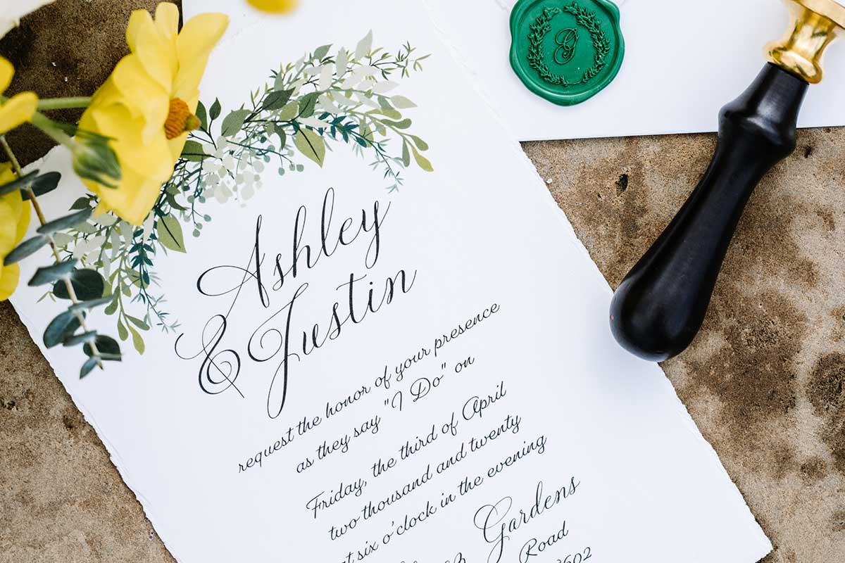 A wedding invitation with green flowers and a wax seal, available at a San Antonio stationery store.